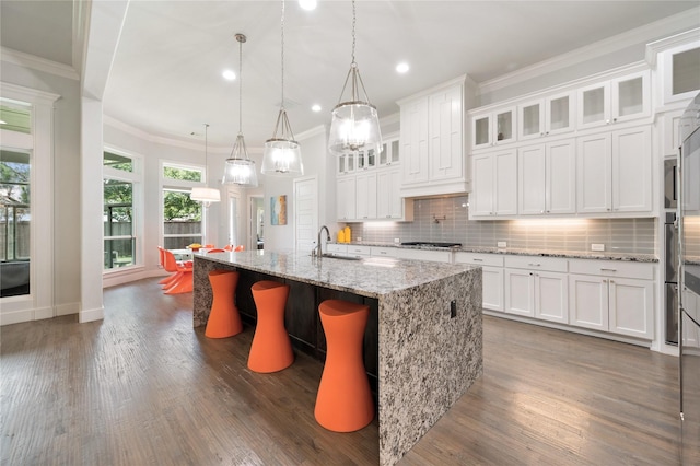 kitchen featuring an island with sink, light stone countertops, white cabinetry, and glass insert cabinets