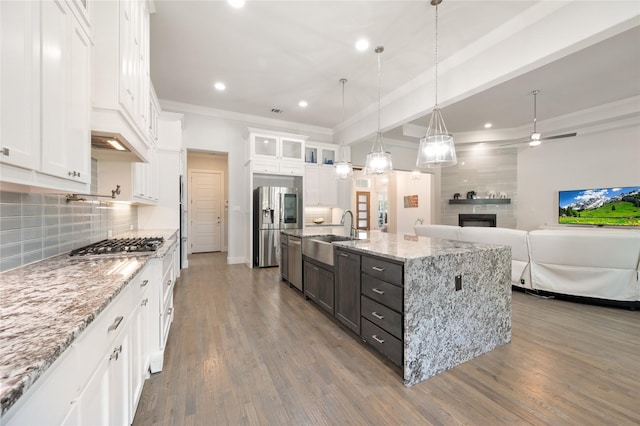 kitchen with hanging light fixtures, glass insert cabinets, open floor plan, white cabinets, and an island with sink