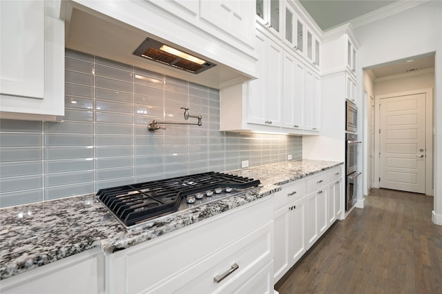 kitchen featuring light stone counters, crown molding, glass insert cabinets, appliances with stainless steel finishes, and white cabinetry