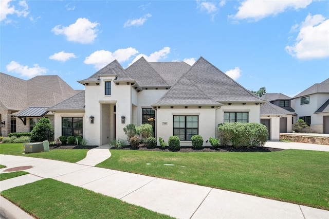 french country style house featuring driveway, roof with shingles, an attached garage, a front lawn, and brick siding