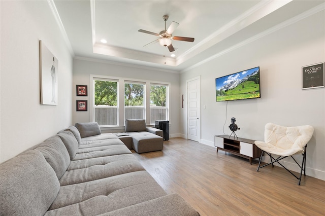 living area featuring light wood finished floors, a tray ceiling, ornamental molding, and baseboards