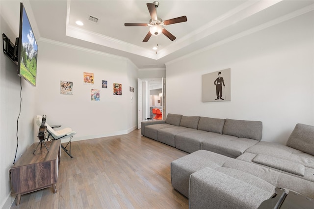 living room with light wood-style floors, visible vents, a raised ceiling, and crown molding