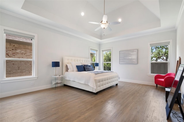 bedroom featuring baseboards, a raised ceiling, a ceiling fan, wood finished floors, and crown molding