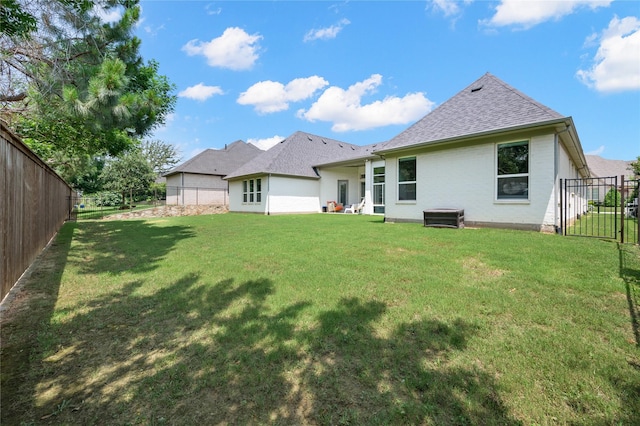 rear view of property featuring a fenced backyard, a shingled roof, and a yard