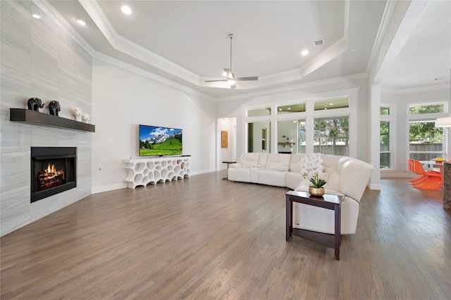 living area featuring a tile fireplace, dark wood-type flooring, visible vents, ornamental molding, and a tray ceiling