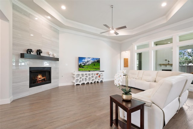 living room with ornamental molding, a raised ceiling, wood finished floors, and a tile fireplace