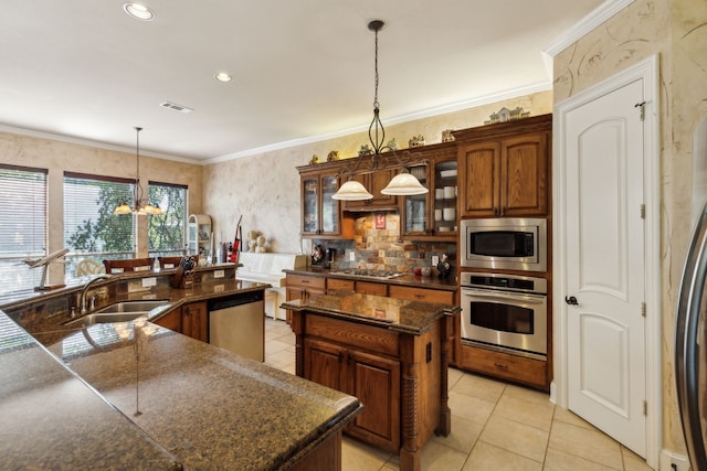 kitchen with pendant lighting, stainless steel appliances, crown molding, and a kitchen island with sink