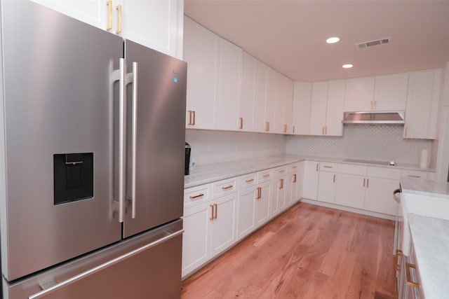 kitchen with stainless steel fridge, black electric stovetop, light hardwood / wood-style floors, white cabinets, and decorative backsplash