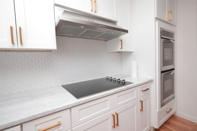 kitchen featuring extractor fan, light stone counters, black electric cooktop, stainless steel double oven, and white cabinets