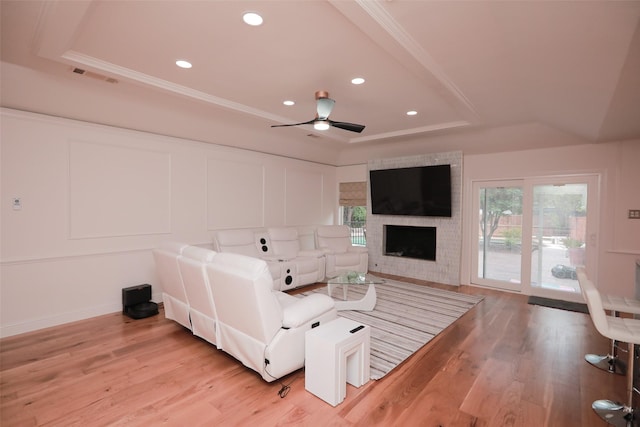 living room featuring light hardwood / wood-style flooring, ornamental molding, a tray ceiling, ceiling fan, and a fireplace