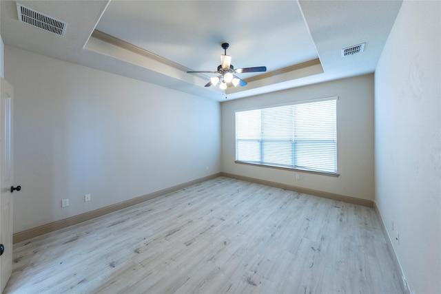 empty room with crown molding, ceiling fan, a tray ceiling, and light hardwood / wood-style flooring