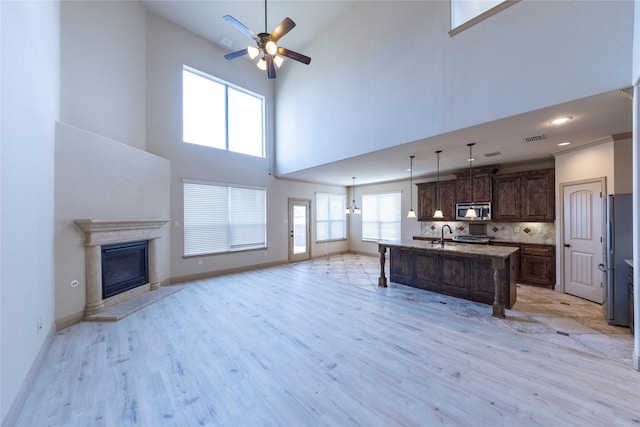 kitchen featuring dark brown cabinetry, tasteful backsplash, a center island with sink, light hardwood / wood-style flooring, and pendant lighting