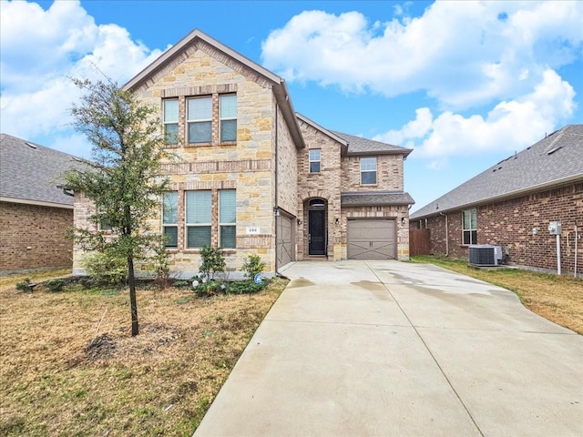 traditional-style house featuring central AC unit, an attached garage, stone siding, driveway, and a front yard