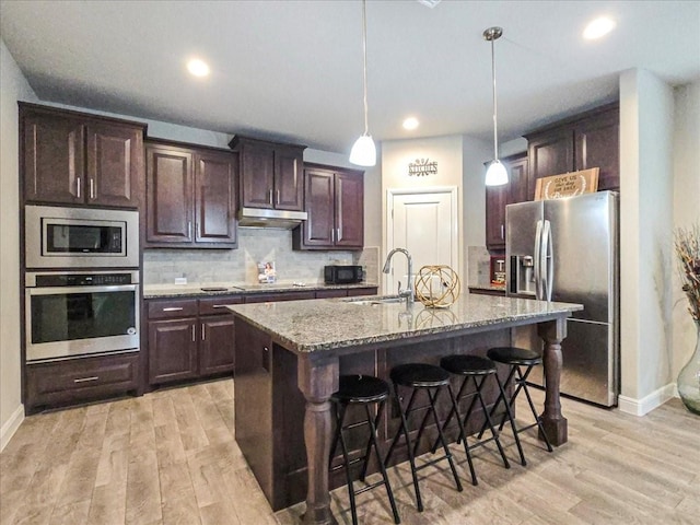 kitchen featuring decorative light fixtures, a center island with sink, a sink, under cabinet range hood, and black appliances