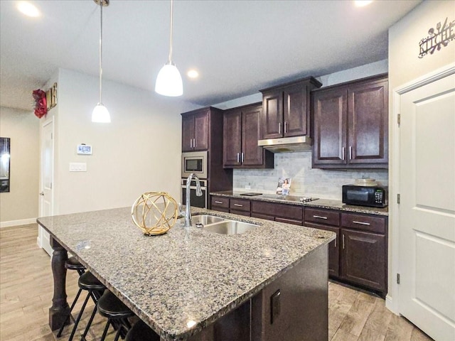 kitchen featuring an island with sink, light stone counters, dark brown cabinets, black appliances, and a sink