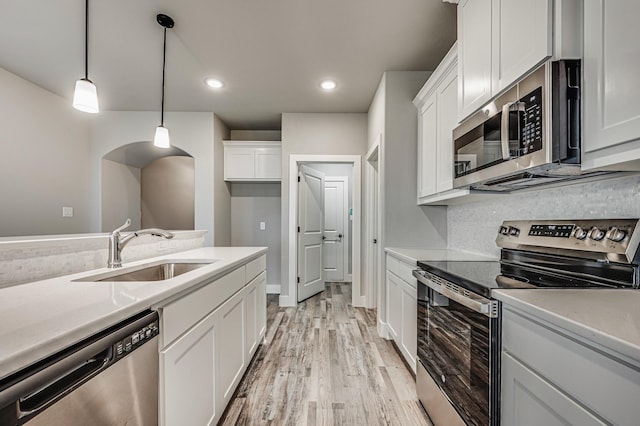 kitchen featuring white cabinets, appliances with stainless steel finishes, hanging light fixtures, light countertops, and a sink