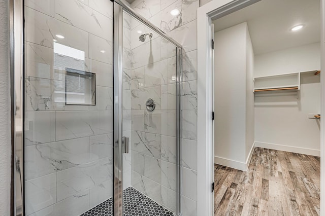 bathroom featuring a stall shower, baseboards, a walk in closet, and wood finished floors