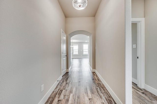 hall featuring arched walkways, light wood-style flooring, and baseboards