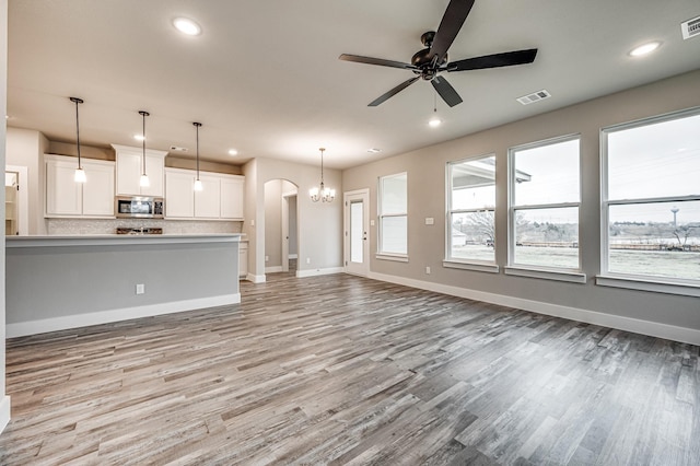 unfurnished living room featuring light wood-type flooring, baseboards, arched walkways, and recessed lighting