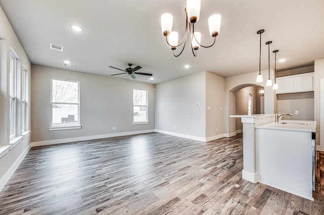 unfurnished living room with arched walkways, visible vents, a sink, wood finished floors, and ceiling fan with notable chandelier