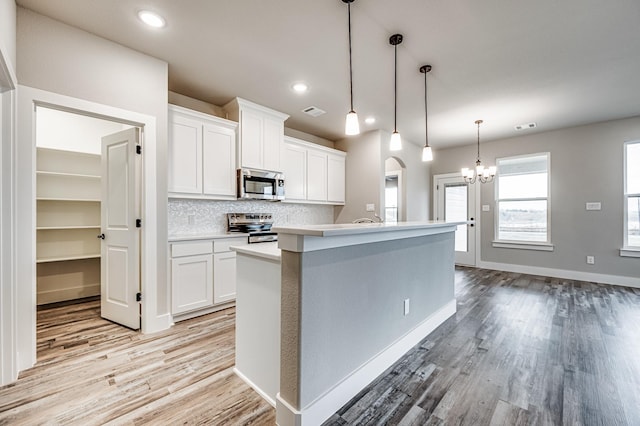 kitchen featuring light countertops, appliances with stainless steel finishes, hanging light fixtures, and white cabinets