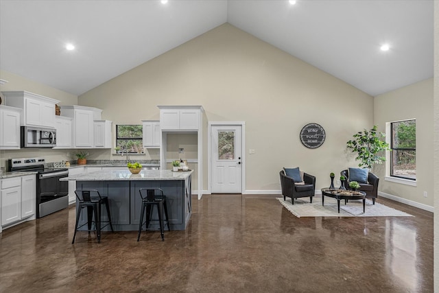 kitchen featuring light stone counters, a center island, stainless steel appliances, white cabinetry, and baseboards