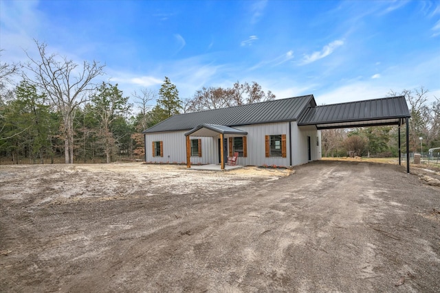 modern farmhouse style home with a standing seam roof, dirt driveway, metal roof, and a carport