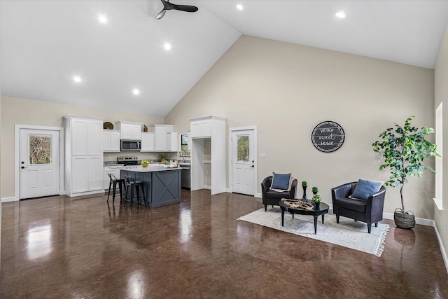 kitchen with concrete flooring, high vaulted ceiling, a kitchen island, white cabinets, and stainless steel microwave