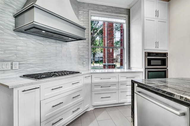 kitchen featuring stainless steel appliances, light stone counters, white cabinets, decorative backsplash, and custom exhaust hood