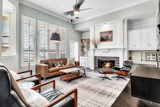 living room with crown molding, built in features, a tile fireplace, hardwood / wood-style flooring, and ceiling fan