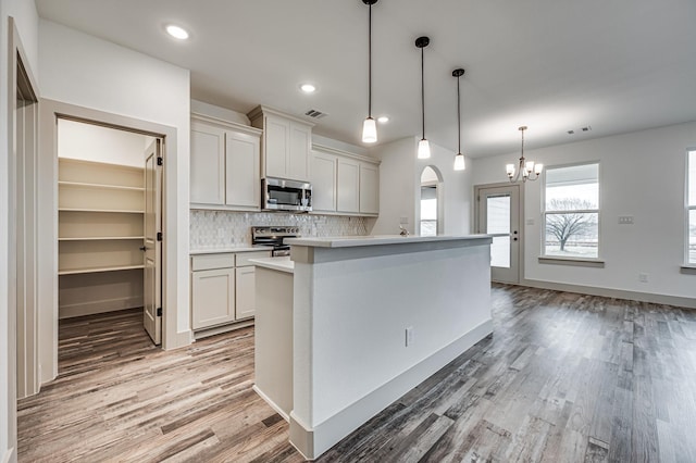 kitchen featuring pendant lighting, light countertops, visible vents, appliances with stainless steel finishes, and a kitchen island with sink