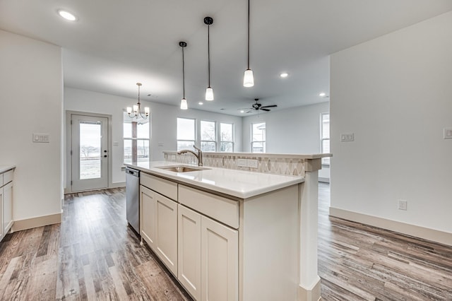 kitchen featuring a kitchen island with sink, a sink, light countertops, dishwasher, and pendant lighting