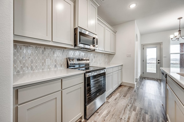 kitchen with pendant lighting, stainless steel appliances, light countertops, decorative backsplash, and light wood-style floors