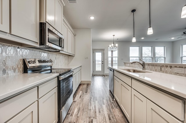 kitchen featuring appliances with stainless steel finishes, light countertops, a sink, and decorative light fixtures