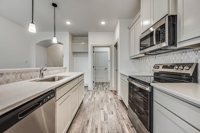 kitchen featuring appliances with stainless steel finishes, hanging light fixtures, a sink, light countertops, and backsplash