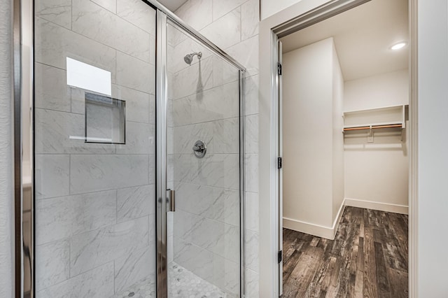 bathroom featuring a stall shower, baseboards, a walk in closet, and wood finished floors