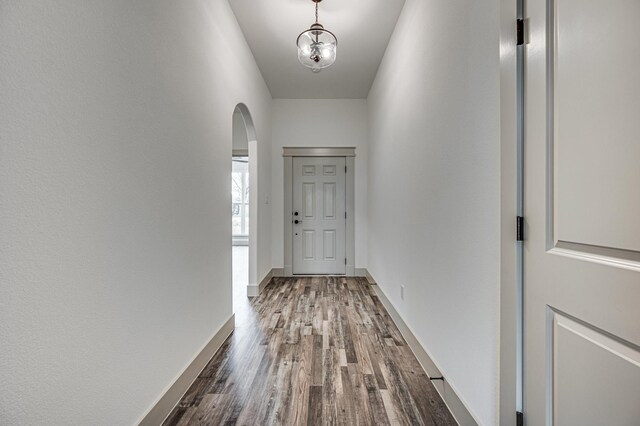 doorway to outside featuring arched walkways, wood finished floors, and baseboards