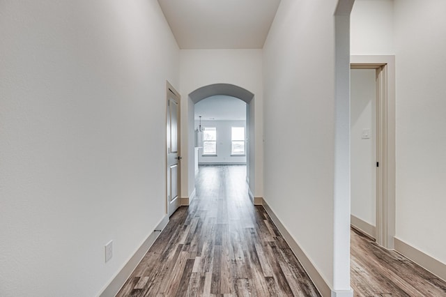 hall with dark wood-style floors, arched walkways, and baseboards