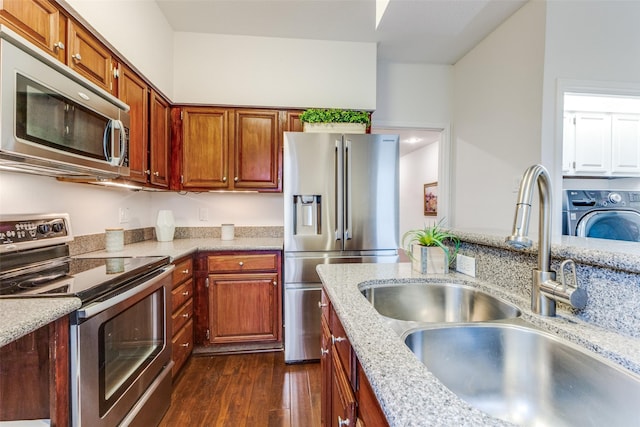 kitchen featuring sink, appliances with stainless steel finishes, dark hardwood / wood-style floors, light stone counters, and washer / dryer