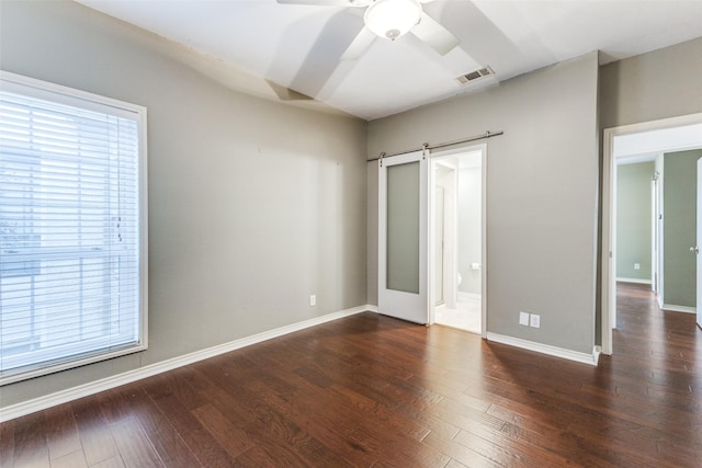 unfurnished bedroom with connected bathroom, dark hardwood / wood-style floors, a barn door, and ceiling fan