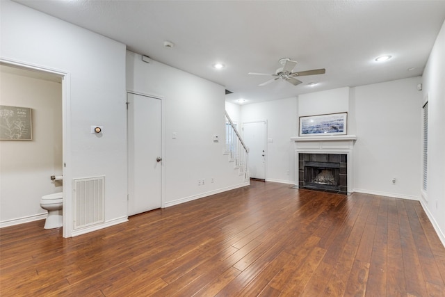 unfurnished living room featuring dark wood-type flooring, ceiling fan, and a tiled fireplace