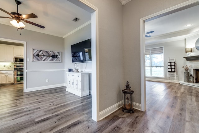 interior space featuring ceiling fan, a fireplace, ornamental molding, and wood-type flooring