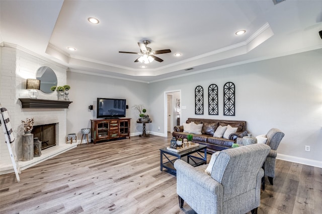 living room featuring crown molding, hardwood / wood-style flooring, ceiling fan, a tray ceiling, and a fireplace