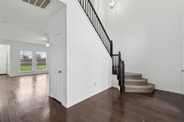 staircase with ceiling fan, a towering ceiling, and hardwood / wood-style floors