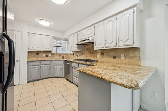 kitchen with appliances with stainless steel finishes, kitchen peninsula, light stone countertops, and white cabinets