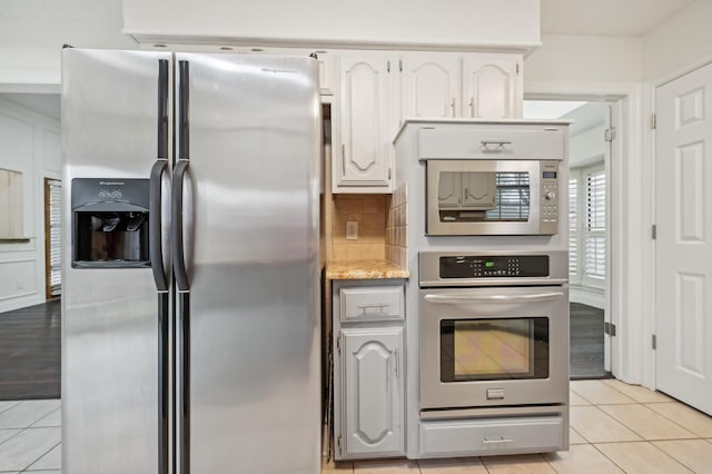 kitchen featuring white cabinetry, light stone counters, tasteful backsplash, light tile patterned floors, and appliances with stainless steel finishes