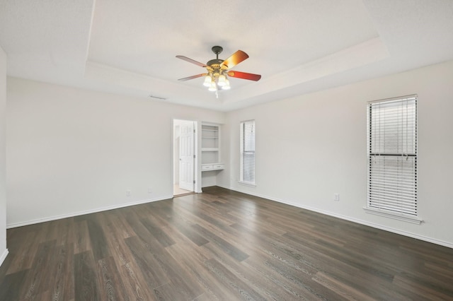 spare room featuring a raised ceiling, dark wood-type flooring, built in features, and ceiling fan