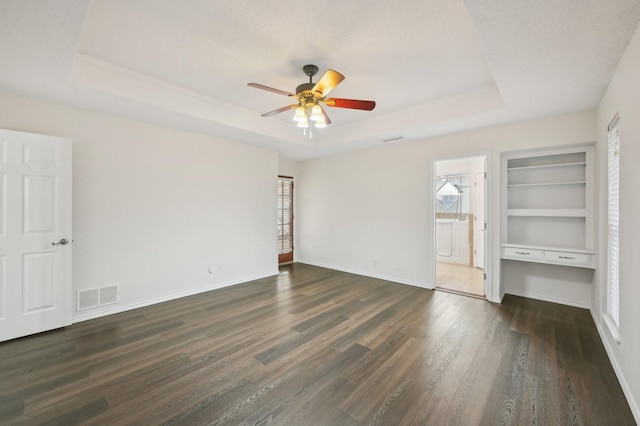 unfurnished bedroom featuring multiple windows, connected bathroom, a tray ceiling, and dark hardwood / wood-style flooring