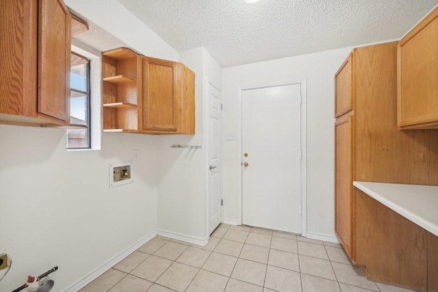 washroom with cabinets, hookup for a washing machine, a textured ceiling, and light tile patterned floors