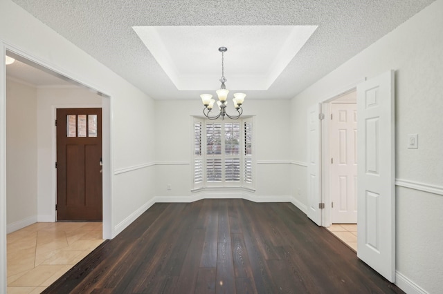 unfurnished dining area with dark hardwood / wood-style flooring, a tray ceiling, a chandelier, and a textured ceiling